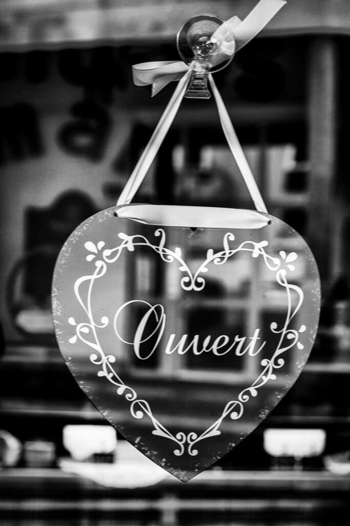 Photographie noir et blanc d'un coeur sur lequel il est écrit ouvert, accroché à la porte d'une boutique. Photo prise par Laure Cartel.