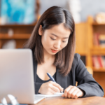 Une femme prend des notes manuscrites pendant qu'elle suit un MOOC en ligne depuis son ordinateur portable.