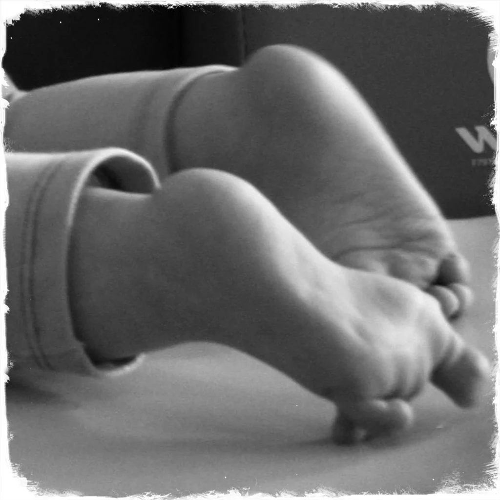 Une photo en noir et blanc de deux pieds de bébé qui est sur le ventre. on voit bien l'accroche des orteils sur le sol nécessaire pour ramper.